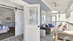 En inglasad veranda med en säng, en sittgrupp med kuddar och en dörr som leder till ett sovrum.