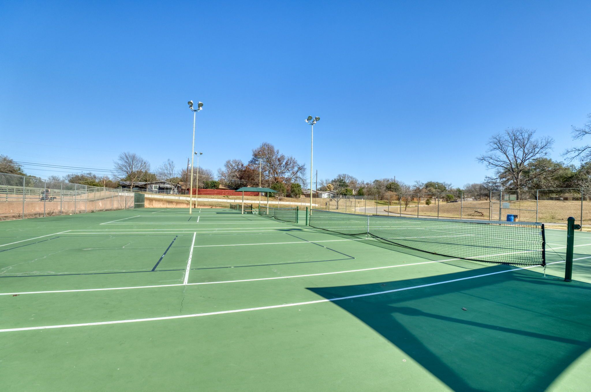An outdoor tennis court with a green surface, net, and floodlights.