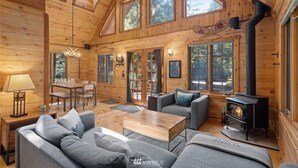 A cozy log cabin interior with a fireplace, wooden furniture, and large windows. - Perfect chalet accommodations tucked into the most wonderful towering trees! (Deming)