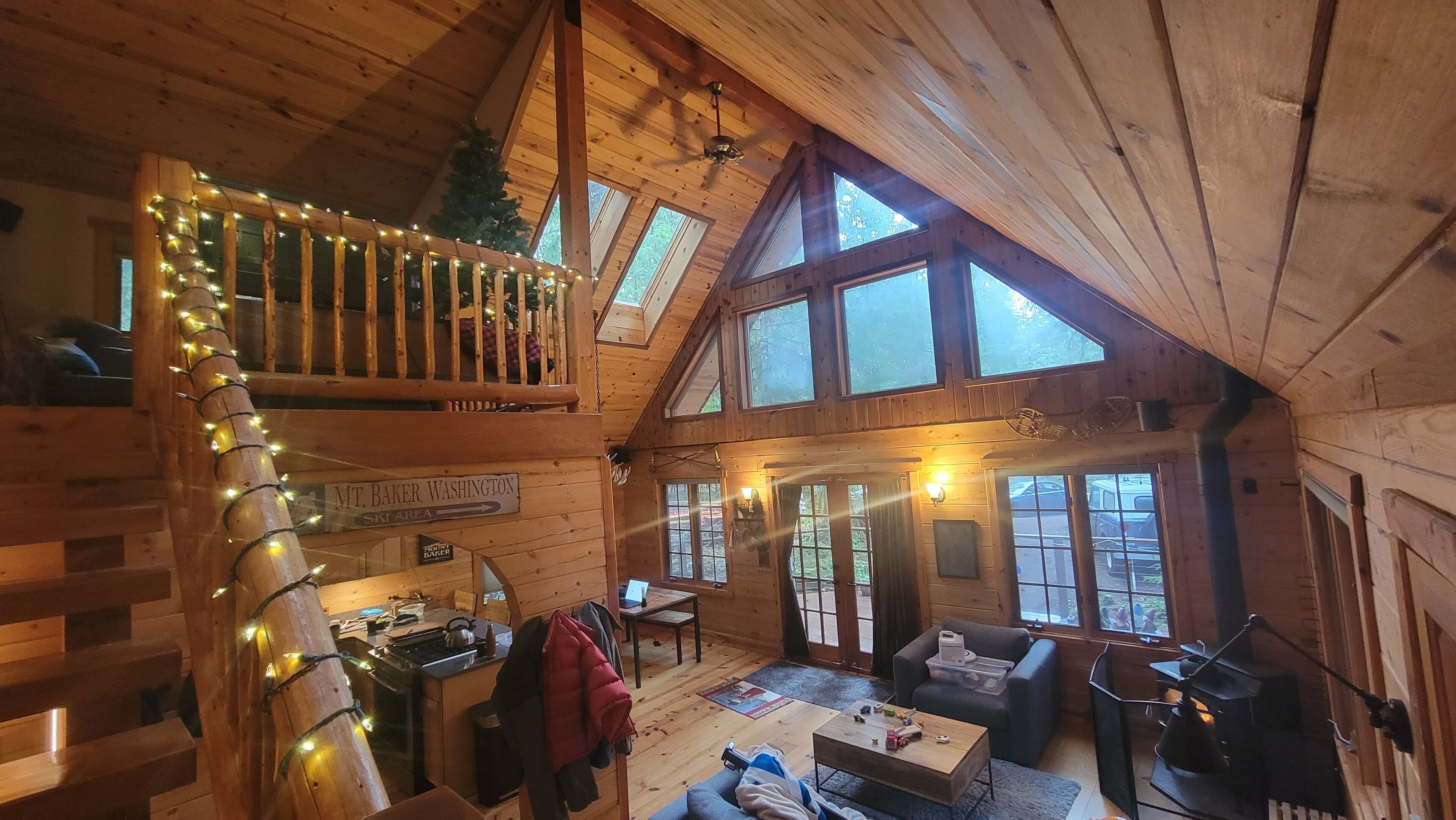 Una cabaña acogedora con interior de madera, una escalera con luces de adorno y un rincón de comedor, con vistas al exterior.