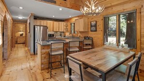 A wooden cabin interior with a kitchen, dining area, and a large window. - Perfect chalet accommodations tucked into the most wonderful towering trees! (Deming)