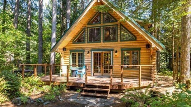 A log cabin with a porch, surrounded by forest. - Perfect chalet accommodations tucked into the most wonderful towering trees! (Deming)