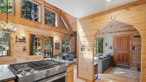 A log cabin with a kitchen area, a dining space, and a living area with a fireplace. - Perfect chalet accommodations tucked into the most wonderful towering trees! (Deming)