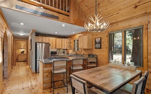 A wooden cabin interior with a kitchen, dining area, and a large window.