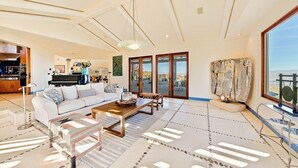 Ein geräumiges Wohnzimmer mit einer großen Couch, einem Couchtisch und Meerblick durch große Fenster.