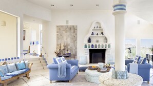 Ein geräumiges Wohnzimmer mit Kamin, blauen Sofas und Blick ins Freie.