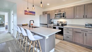 A modern kitchen with a central island, bar stools, stainless steel appliances, and pendant lighting. - Grand Junction Home ~ 1 Mi to Downtown (Grand Junction)