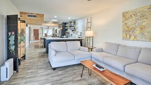 Un salon moderne avec un canapé d’angle, une table basse en bois et une cuisine en arrière-plan.