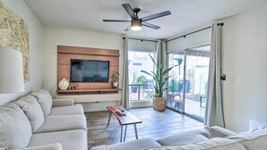 Un salon moderne doté d’un téléviseur à écran plat, d’un ventilateur de plafond et d’une porte-fenêtre coulissante donnant sur un espace extérieur.