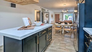 Une cuisine moderne dotée d’un îlot central, de poutres en bois au plafond et d’un coin repas avec une table et des chaises en bois.