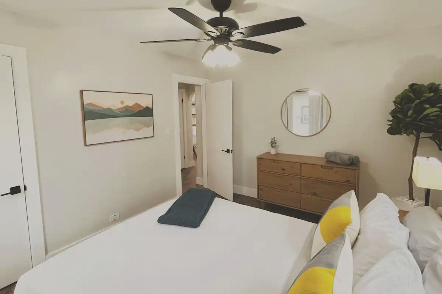 Ein Schlafzimmer mit einem Bett, einem Deckenventilator, einem Schminktisch, einem Spiegel und einer Tür zu einem anderen Raum.