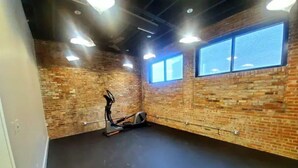 Een kamer met bakstenen muren, een groot raam en fitnessapparatuur.