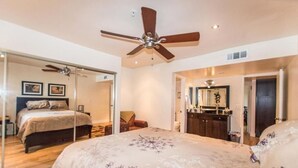 A bedroom with a bed, a ceiling fan, a bathroom with a mirror, and a door leading to another room. - Top Floor Condo Minutes from Old Town (Scottsdale)