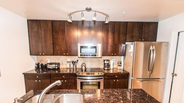A modern kitchen with dark wooden cabinets, stainless steel appliances, granite countertops, and a built-in oven. - Top Floor Condo Minutes from Old Town (Scottsdale)