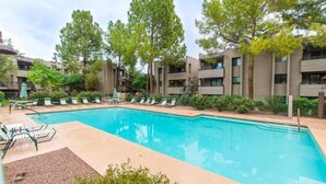 A swimming pool with lounge chairs and a small deck area, surrounded by trees and a building with multiple balconies. - Top Floor Condo Minutes from Old Town (Scottsdale)