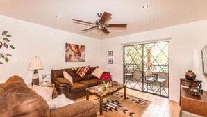 A living room with a brown sofa, a coffee table, a ceiling fan, and a large window with a view of the outdoors. - Top Floor Condo Minutes from Old Town (Scottsdale)