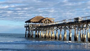 Une jetée surmontée d’une structure à toit de chaume et dotée d’une passerelle en bois qui s’avance dans l’océan.