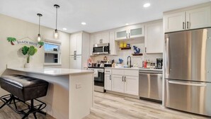 Une cuisine moderne avec des meubles blancs, des appareils en acier inoxydable et un coin bar agrémenté d’un tabouret en cuir.
