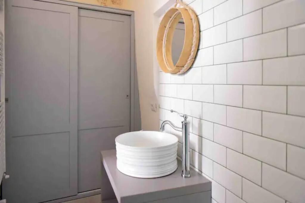 Un bagno con un lavandino bianco rotondo, uno specchio e una parete rivestita di piastrelle.