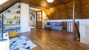 A spacious loft with a high ceiling, wooden beams, a built-in bookshelf, a sofa, and a dining table.