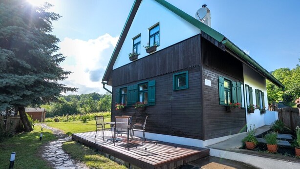 A two-story house with a sloped roof, a deck with outdoor furniture, and a satellite dish on the roof.