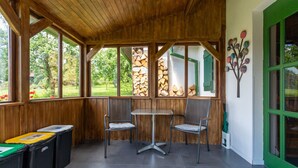 A covered outdoor seating area with a table and chairs, wooden beams, large windows, and a green door.