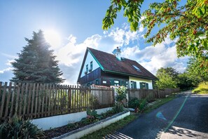 Een huis met een schuin dak, schoorsteen en een omheinde tuin met planten.
