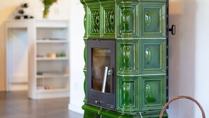 A green, ornate stove with a glass door, a white shelving unit in the background, and a wicker basket on the floor.