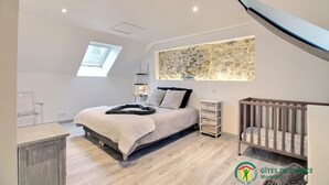 A bedroom with a bed, a crib, a skylight, and a stone wall. - Heol - AMBON - Gîte (AMBON)