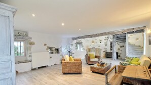 A spacious living area with wicker furniture, a stone wall, and a rustic wooden ceiling. - Heol - AMBON - Gîte (AMBON)