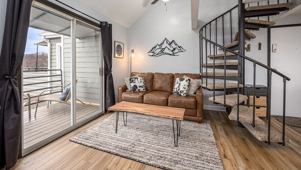 A living room with a brown leather sofa, a wooden coffee table, and a large glass door leading to a balcony. - Incredible Mtn. Views, Indoor & Out Door Pools, Cozy Loft, Minutes to Downtown! (Gatlinburg)