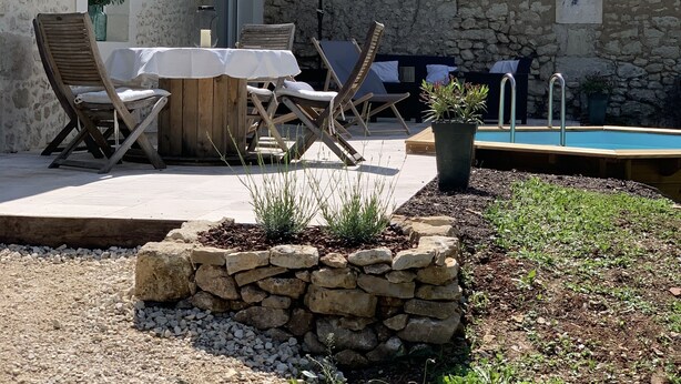 Un patio rústico al aire libre con un muro de piedra, una piscina y una mesa con sillas.