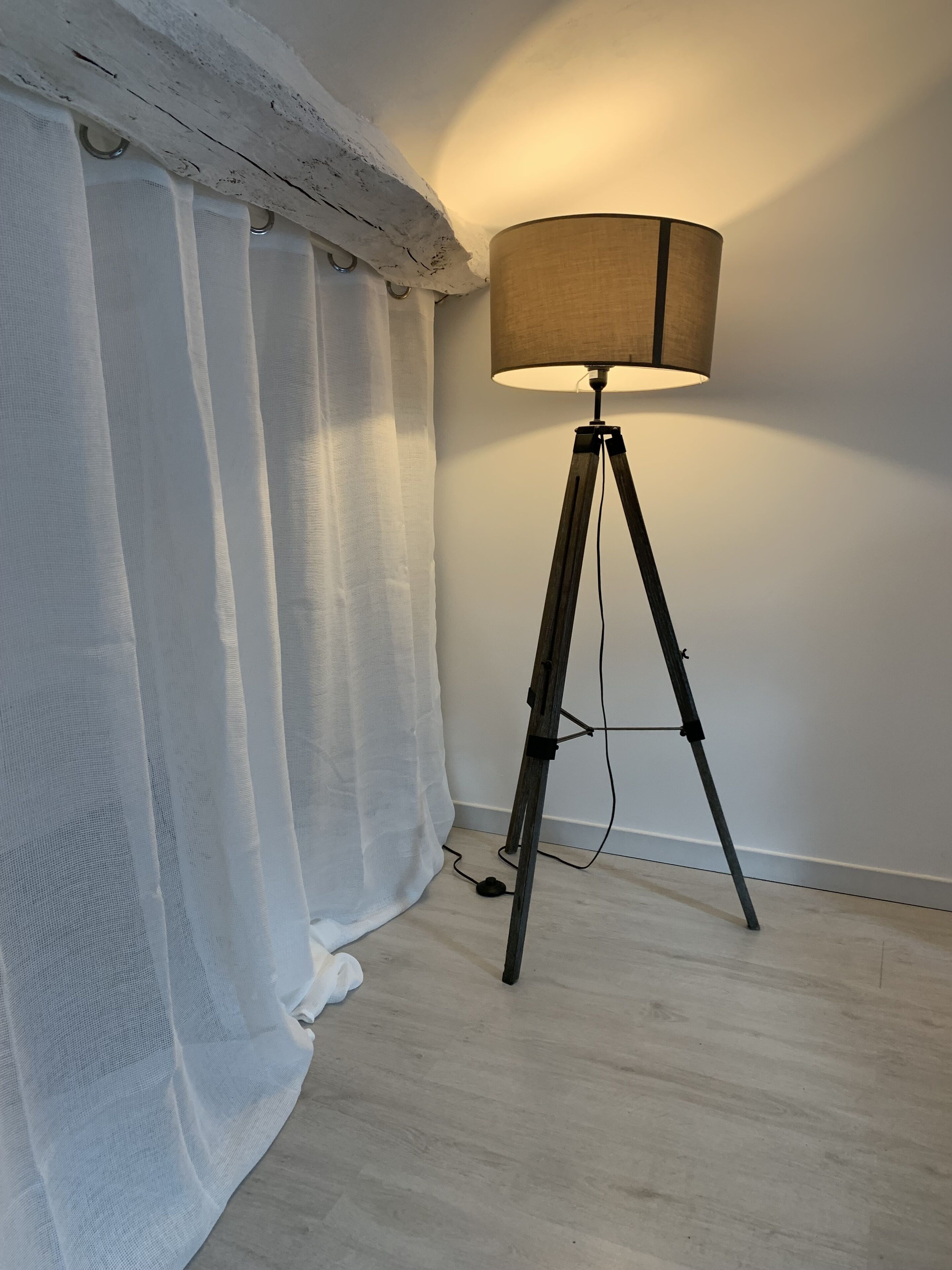 Une lampe sur pied, montée sur un trépied, se trouve dans une pièce dont le sol est en bois et les murs sont blancs.