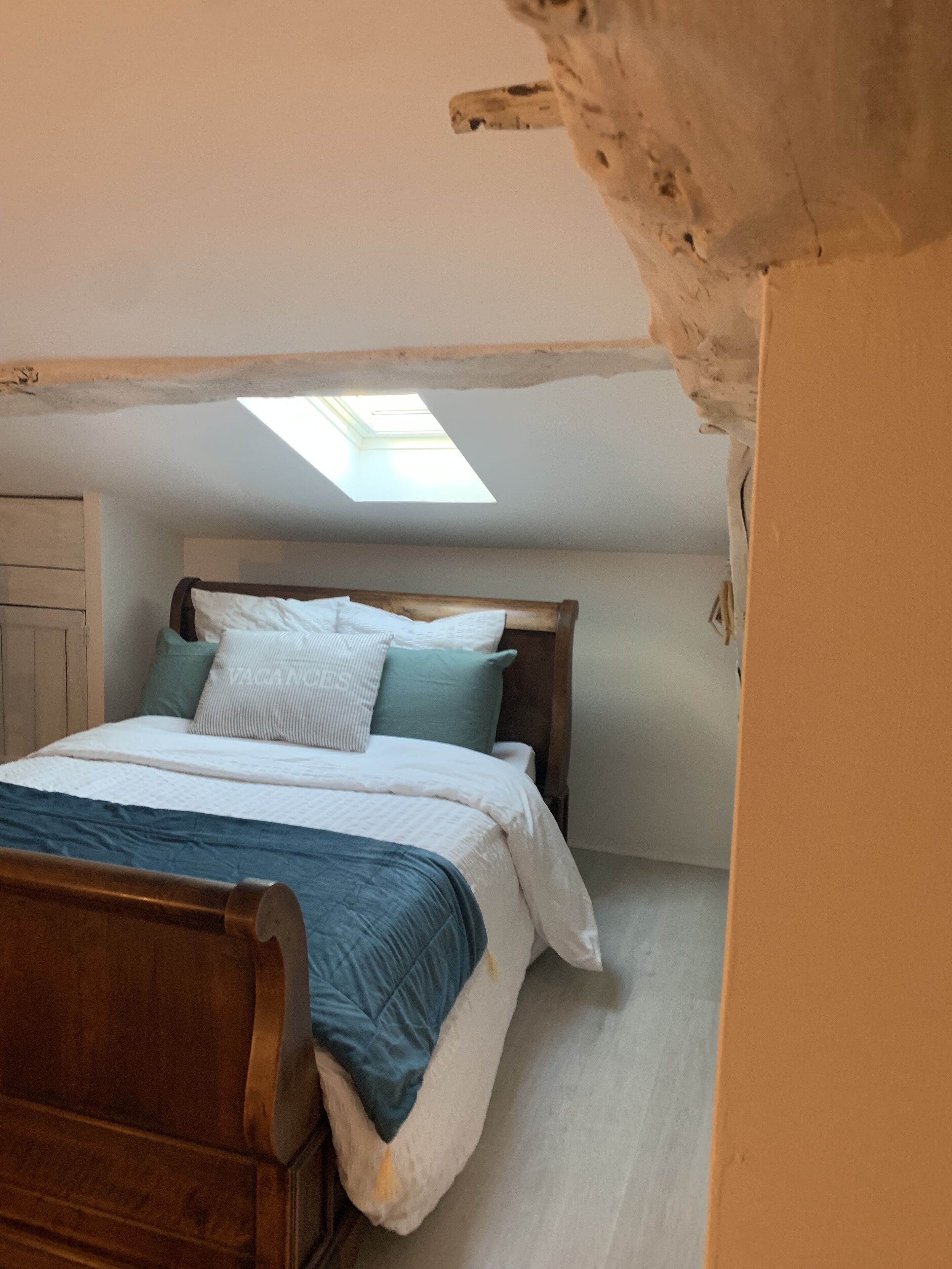 Une chambre avec un puits de lumière, un cadre de lit en bois et une tête de lit blanche.