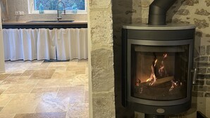 Una chimenea de piedra con puerta de vidrio, una cocina con ventanal y piso de baldosas.