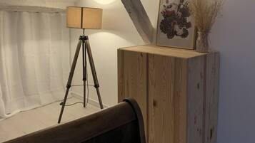 A bedroom with a wooden headboard, a tripod with a lamp, a wooden cabinet with a vase, and a framed picture on the wall.