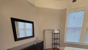 A bedroom with a bed, a dresser, a mirror, a window with blinds, and a ceiling fan. - In Through The Side Door (Victorian District) (Savannah)