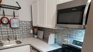 A kitchen with white cabinets, a stainless steel refrigerator, a microwave, a stove, and a sink. - In Through The Side Door (Victorian District) (Savannah)