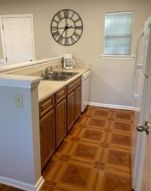 Una cocina con piso de madera, un reloj en la pared y una ventana con persianas.