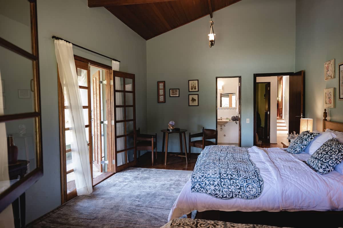 Ein Schlafzimmer mit einem großen Bett, einem kleinen Tisch und einem Stuhl. Es gibt Türen zu anderen Räumen und einem Flur.