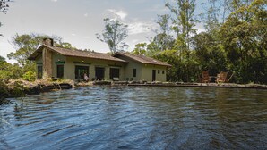 A house by a calm river with a wooden deck and chairs. - Reserva Mata Grande - Nature Park (Biritiba-Mirim)