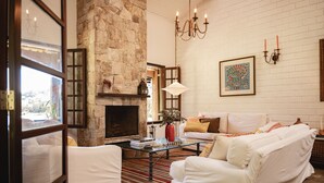 A cozy living room with a stone fireplace, white furniture, and a chandelier. - Reserva Mata Grande - Nature Park (Biritiba-Mirim)