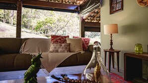 A cozy room with a wooden ceiling, a sofa with a patterned throw, a lamp, and a view of trees outside. - Reserva Mata Grande - Nature Park (Biritiba-Mirim)