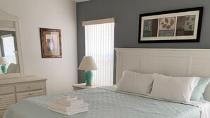 Un dormitorio con cama, mesita de noche, lámpara, cómoda y ventana con persianas.