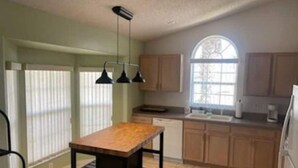 Una cocina con una mesa de madera, un ventanal y armarios de tonos claros.