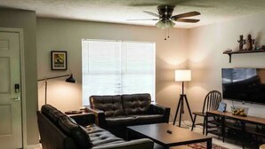 A living room with a sofa, coffee table, TV, and a ceiling fan. - Equilibrium (Islands Bungalow) (Savannah)