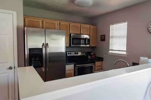 Compact kitchen with modern appliances, refrigerator, microwave, and oven, featuring wooden cabinets and a white countertop.