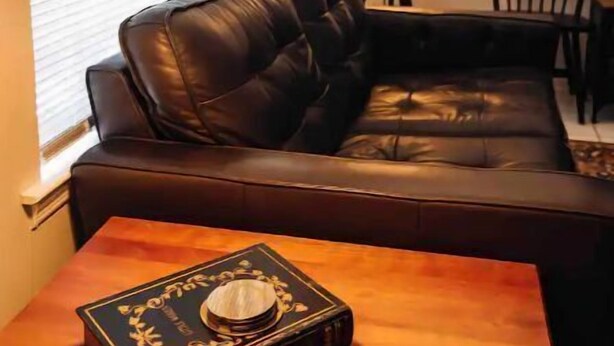A cozy living room with a leather sofa, a wooden coffee table with a decorative book, a floor lamp, and a chair. - Equilibrium (Islands Bungalow) (Savannah)