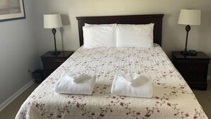 A neatly made bed with a floral bedspread, two white pillows, and two folded towels on the bed. - Equilibrium (Islands Bungalow) (Savannah)