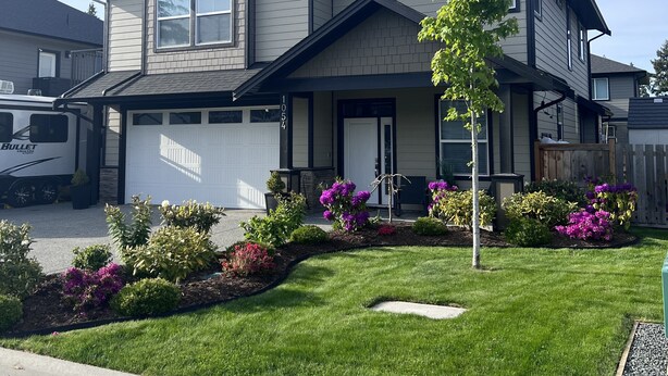 A two-story house with a garage, a driveway, and a well-maintained lawn with colorful flowers.